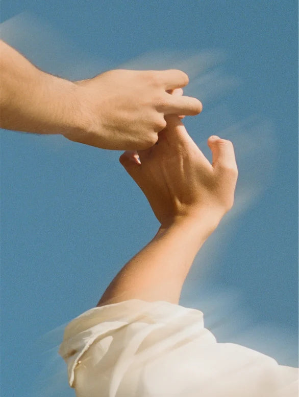 Two hands holding each other with blue sky background.
