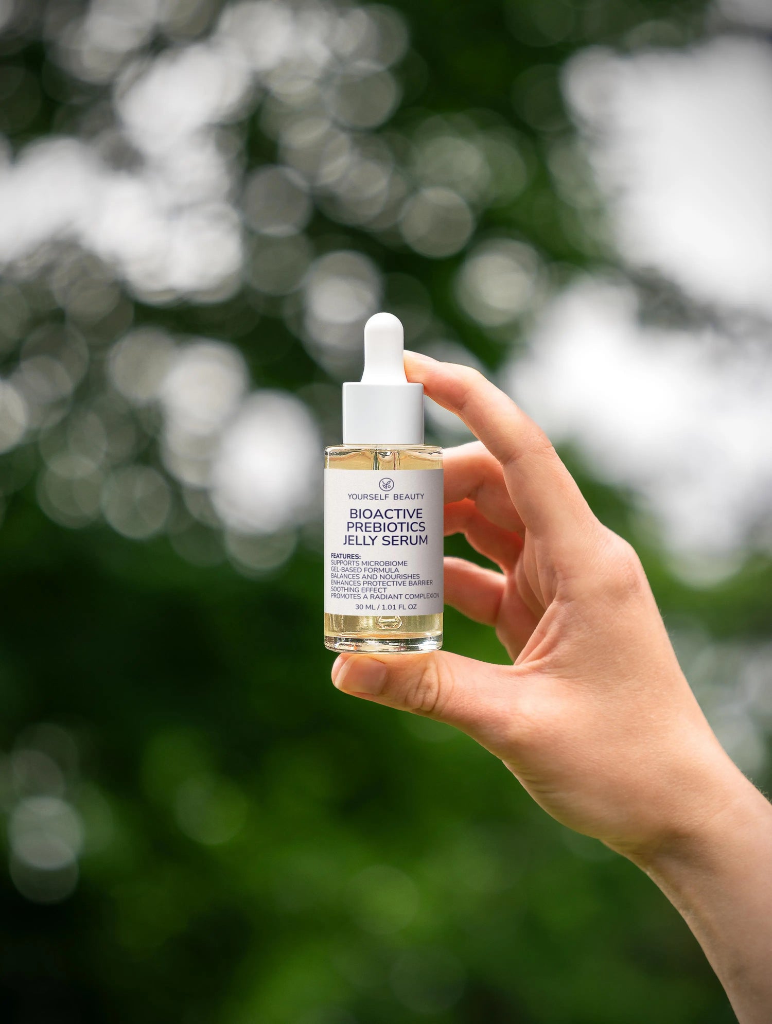 Hand holding a bottle of Probiotic Jelly Serum with a blurred green background.