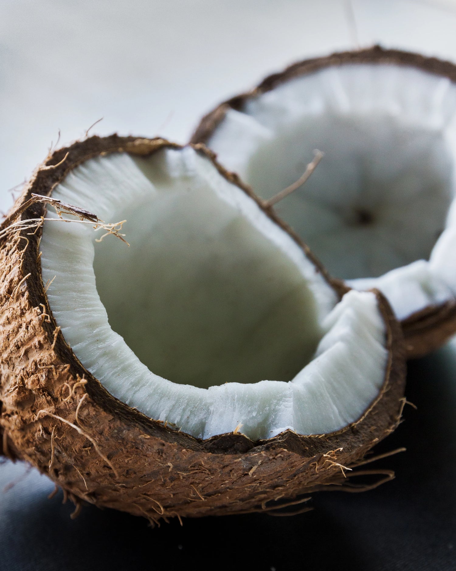 Close-up of a halved coconut on a dark surface with a light background.