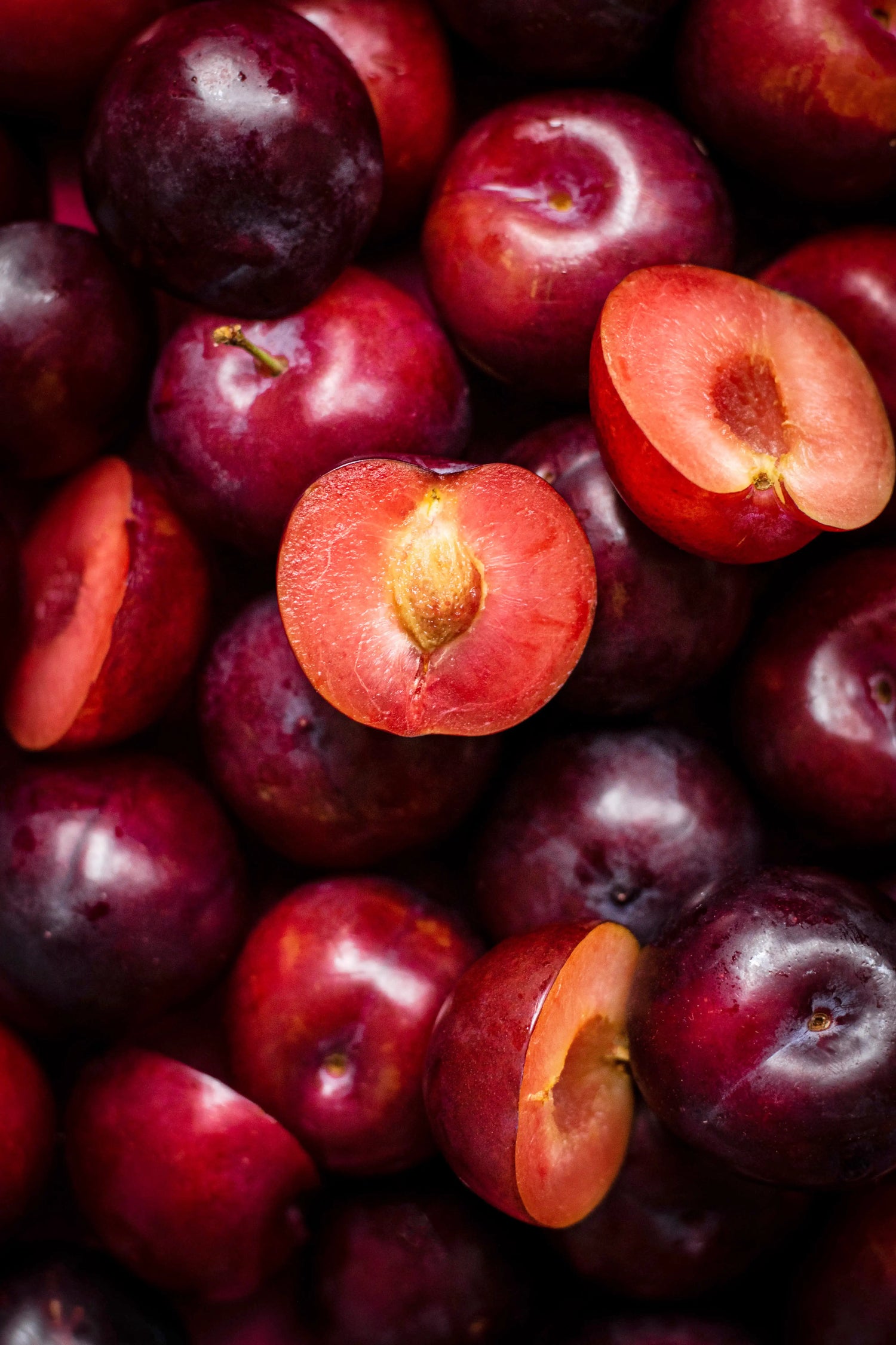 Close-up of plums with a halved plum showing the interior.