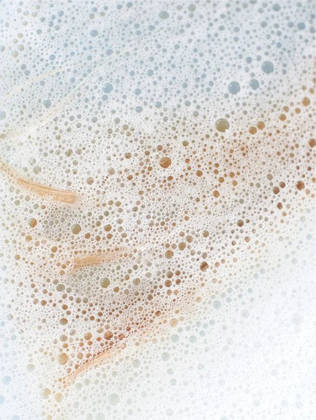 Close-up of shampoo bubbles on a white background with blond hair.